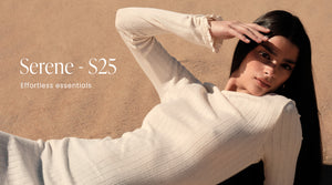 En modell ligger i en ribbet, kremhvit "Almond White Pointelle Beach Dress" på en sandfarget bakgrunn ved stranden i et varmt og solrikt miljø. Banneret inneholder også teksten "Serene - S25" og "Effortless essentials".