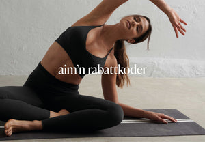 En modell i svart treningstøy utfører en sidestrekk på en yogamatte, med lukkede øyne og et rolig uttrykk. Teksten "aim'n rabattkoder" vises til høyre.